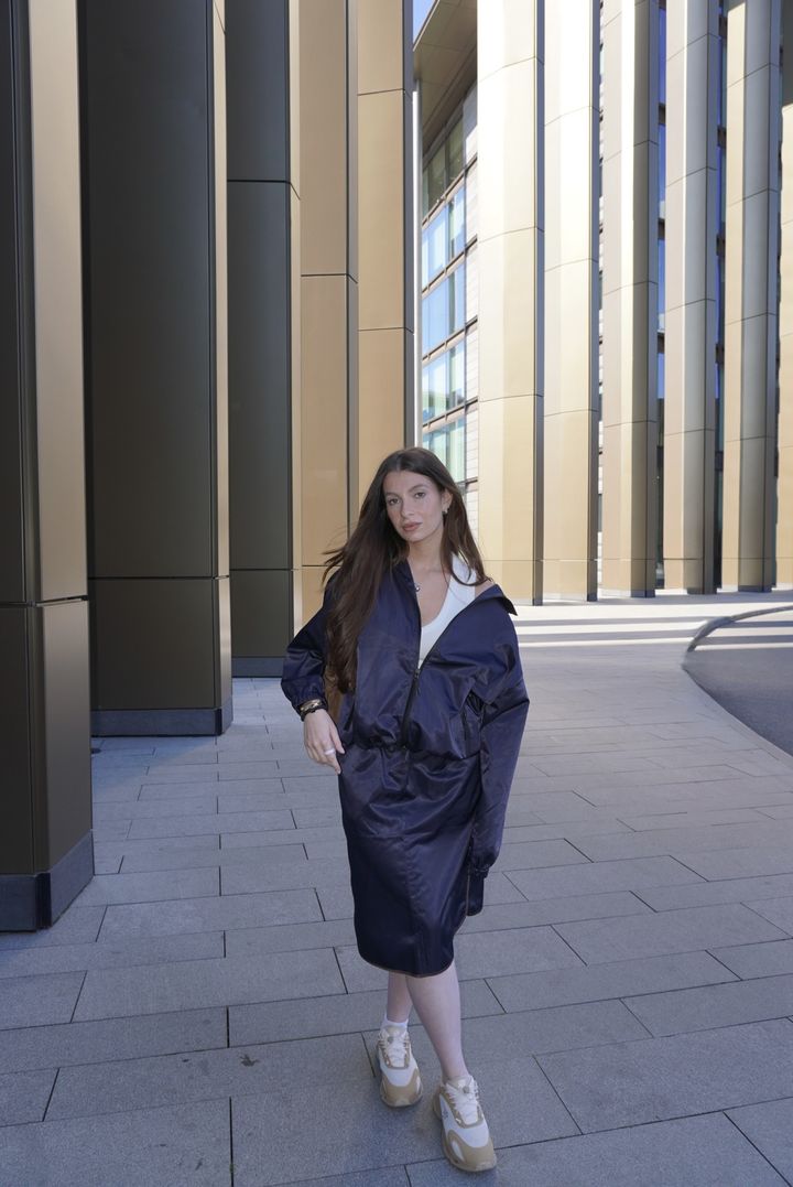 A navy satin jacket and matching midi skirt over a white tank, among bronze columns