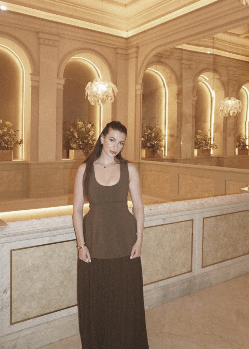Adele in an olive column dress beneath the lit arches of a marble hall